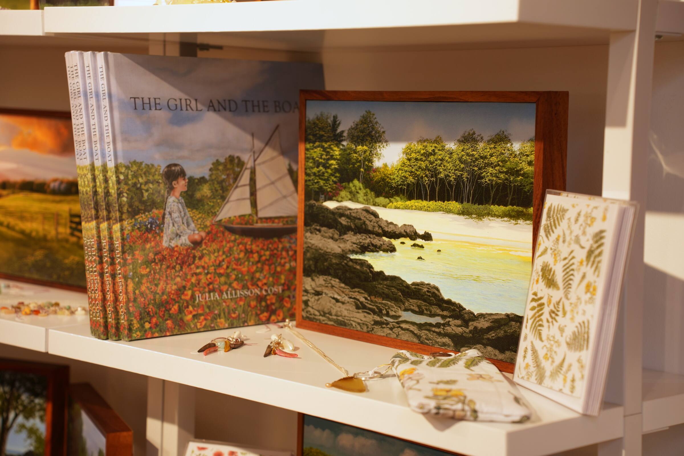 Books, a framed painting and gifts on a white shelf