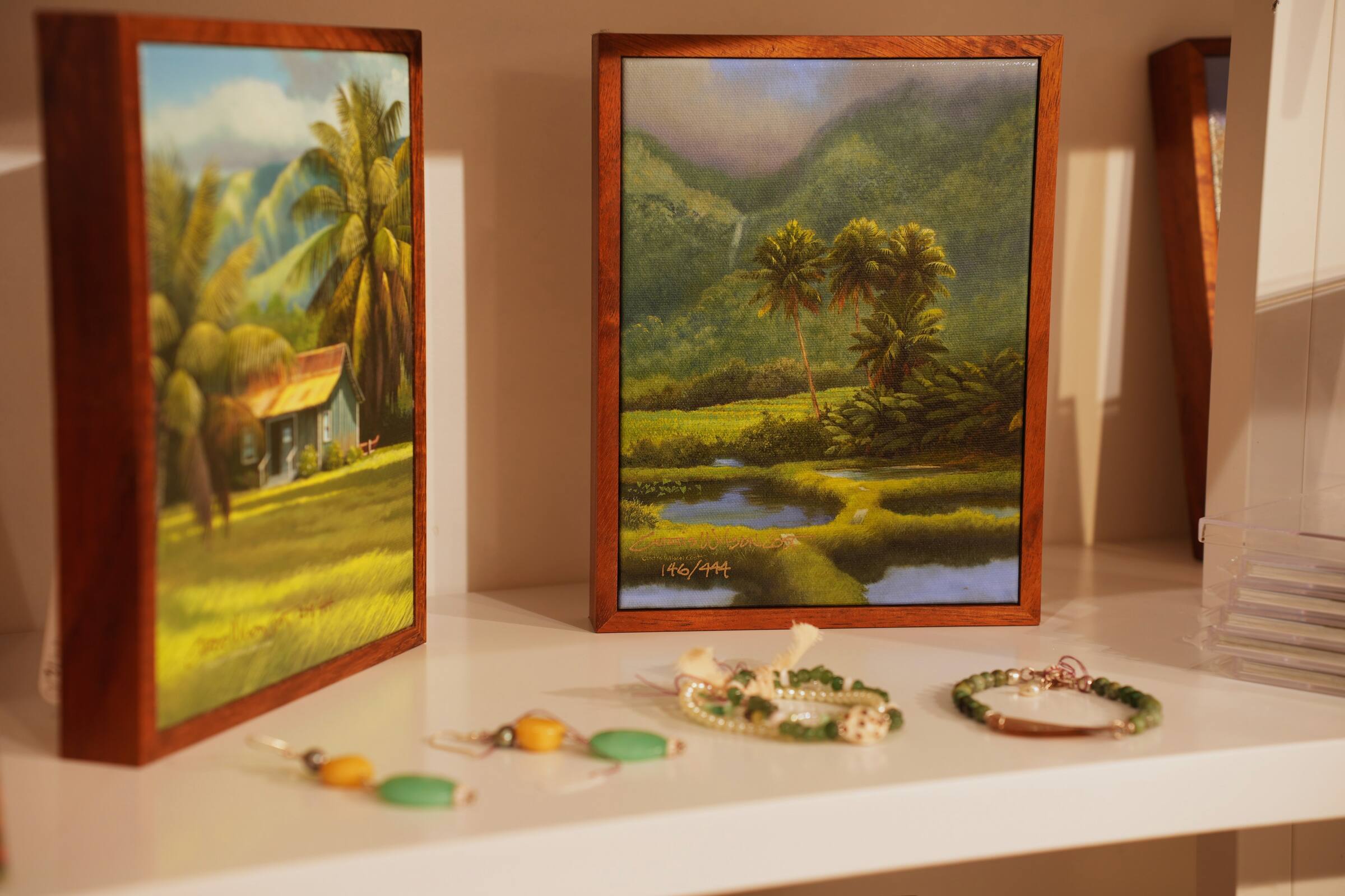 Small paintings in koa frames on a shelf with handmade bracelets