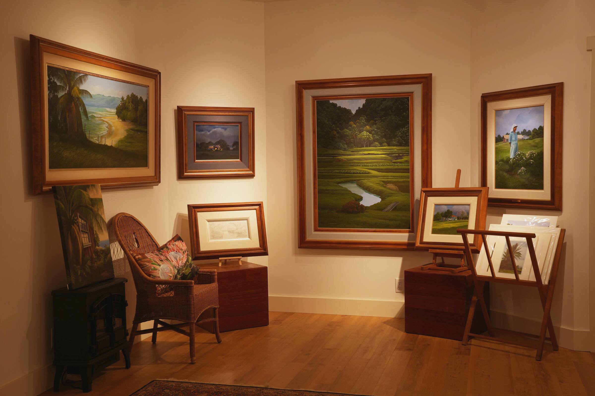 A corner of the gallery: framed paintings, a wicker chair and a print rack