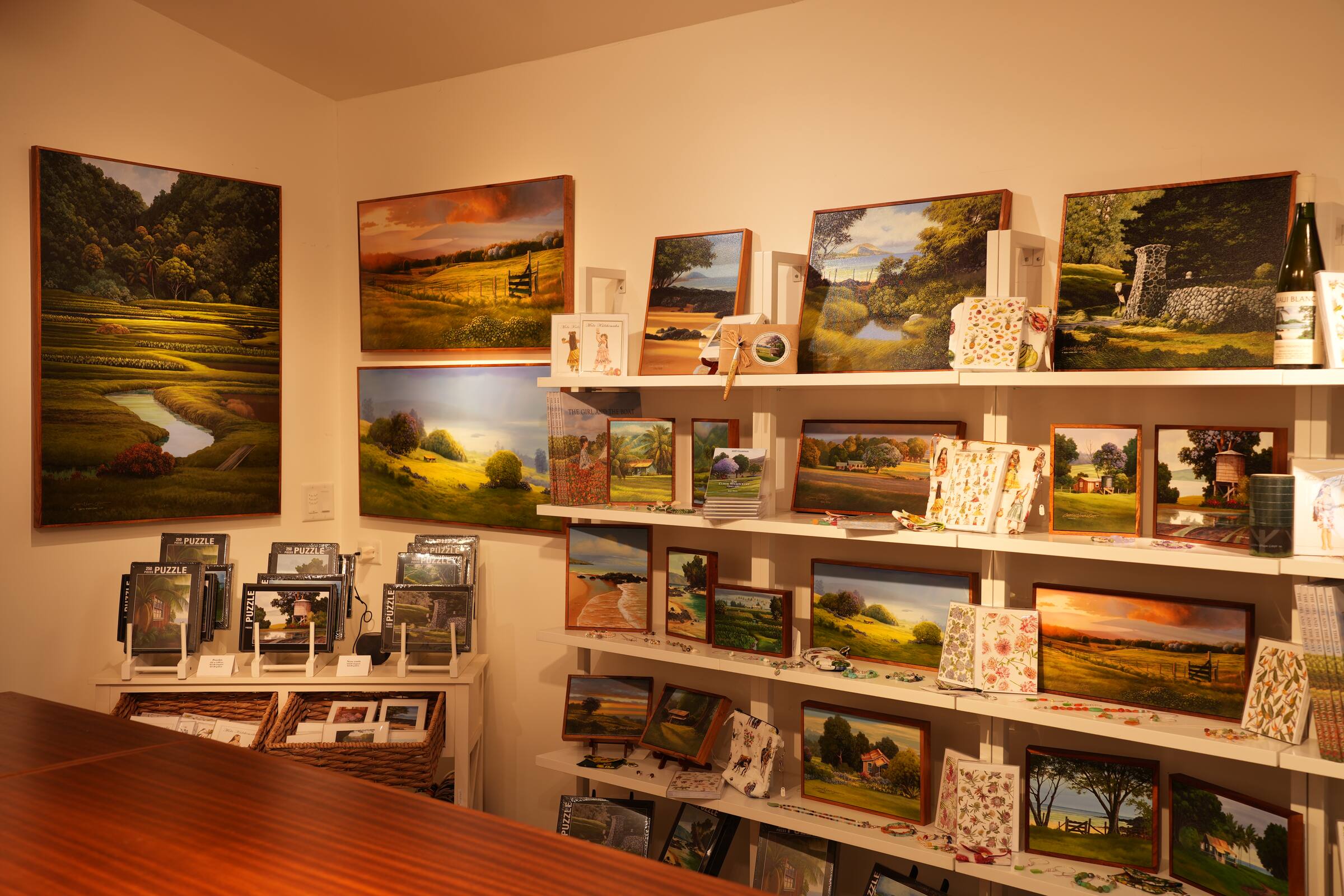 Shelves of small paintings, cards and puzzles beneath larger paintings on the walls