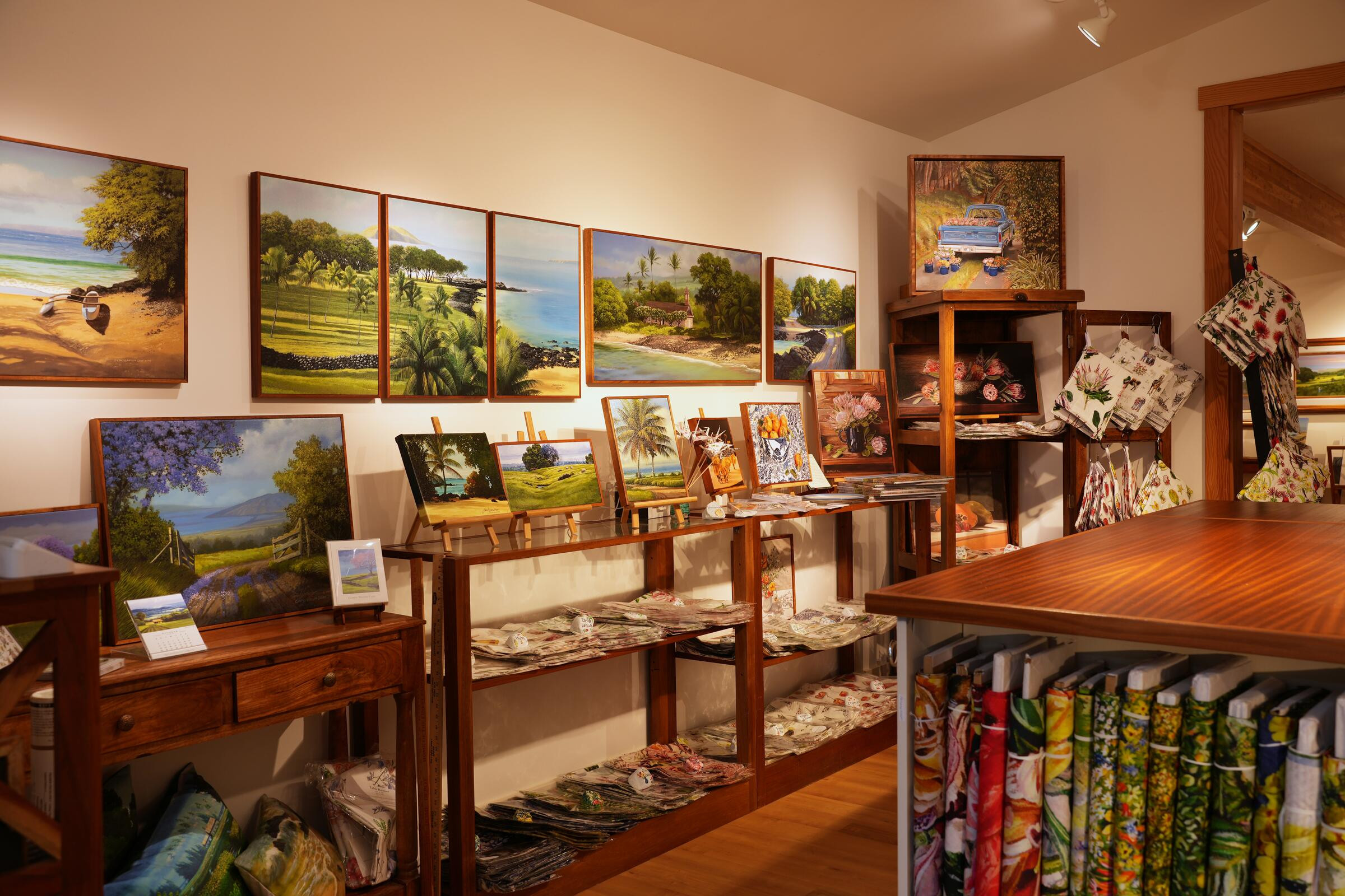 Paintings on the gallery walls above shelves of small paintings, cards and fabrics